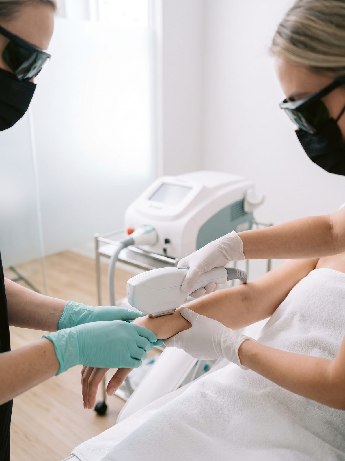 Gloved hands holding a laser handpiece over a client's arm